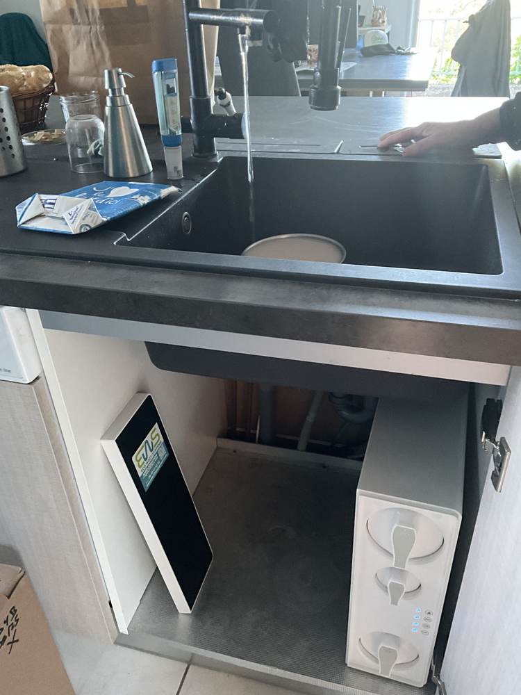 Osmoseur placé dans un meuble de cuisine en bois clair, sous un évier deux bacs